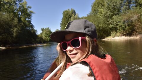 Paddeln auf dem Fluss Kind mit Sonnenbrille sitzt lachend im Kanu auf einem Fluss