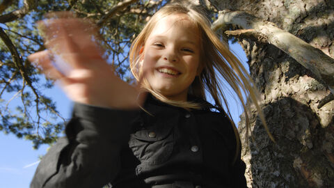 Hallo! Ein lachendes Kind winkt in die Kamera. Es ist draußen in der Natur