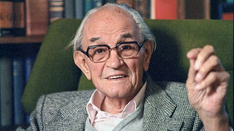 Portrait von Martin Niemöller in Sessel vor Bücherwand.