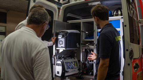 Ministerpräsident Rhein steht vor dem geöffneten Einsatzwagen, zwei weitere Personen erklären Gerätschaften.