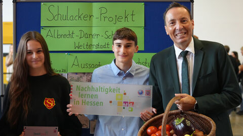 Umweltstaatsekretär Oliver Conz und Kultusstaatssektretär Dr. Manuel Lö-sel ehren Engagement für Nachhaltigkeit, Klima- und Umweltschutz Bildtext: Schulacker Projekt. Nachhaltigkeit lernen in Hessen. Umweltstaatsekretär Oliver Conz und zwei Schüler lächeln in die Kamera. Übergabe der "Umweltschule".