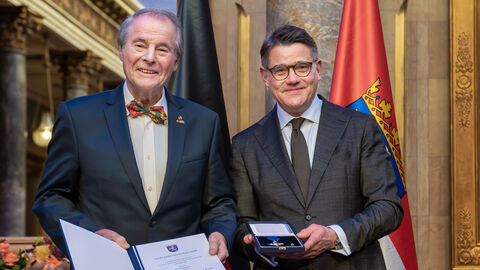 Zwei Personen stehen nebeneinander und halten die Auszeichnung hoch.