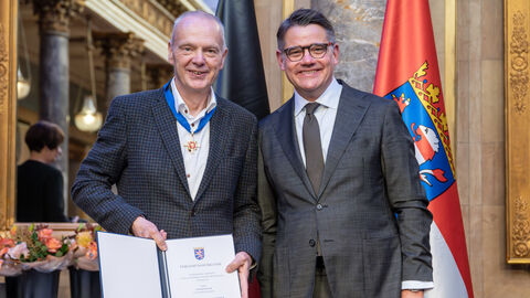 Zwei Personen stehen nebeneinander und halten die Auszeichnung hoch.