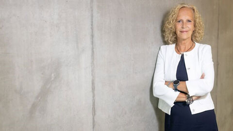 Frau mit blonden Haaren steht vor Betonwand.