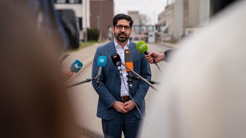 Wirtschaftsminister Mansoori steht in einer Interviewsituation vor Mikrofonen und spricht.