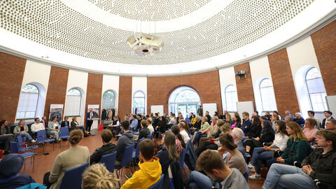 Die Veranstaltung fand im Gießhaus der Universität Kassel statt Großer, runder Saal mit Menschen, die auf Stühlen sitzen.