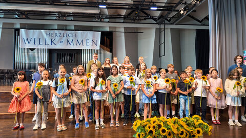 Schulbeginn Frankfurter Lessing-Gymnasium  Viele Schülerinnen und Schüler halten Sonnenblumen in den Händen. Auf einem Banner steht "Herzlich Willkommen"