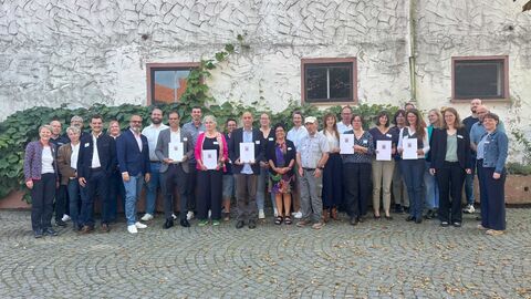 Staatssekretär Daniel Köfer steht mit den Bescheidempfängerinnen und Bescheidempfängern zum Gruppenbild zusammen.