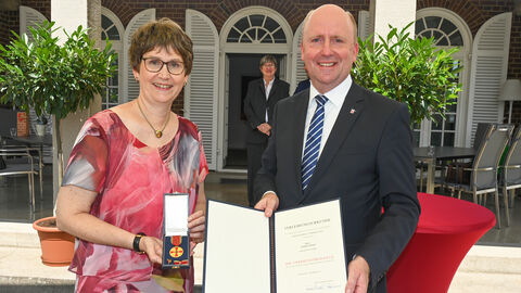 Verdienstmedaille für Marion Beier aus Frankfurt am Main Marion Beier und Europastaatssekretär Uwe Becker halten Verdienstmedaille und Urkunde in die Kamera