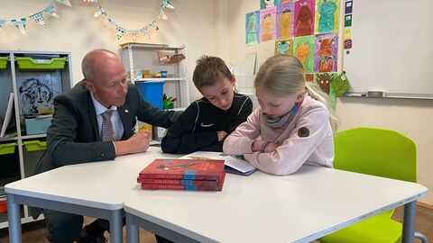 Deutschstunde in Grundschule Kultusminister Schwarz sitzt gemeinsam mit Schüler und Schülerin an Tisch und schaut in ein Buch