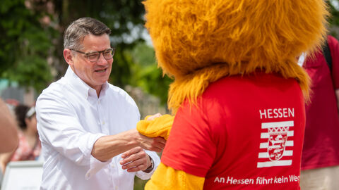 Ministerpräsident Rhein schüttelt dem Löwen-Maskottchen des Landes die Hand.