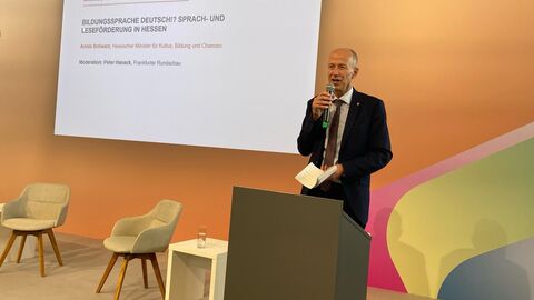 Mann steht auf einer Bühne und spricht in ein Mikrofon.