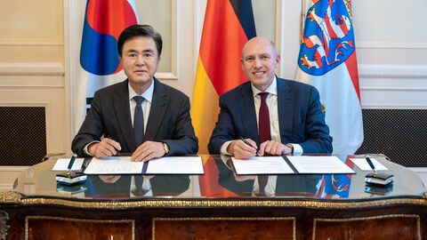 Staatsminister Manfred Pentz mit dem Gouverneur der Region Chungnam, S.E. Taeheum KIM, bei der Unterzeichnung des MoU  Zwei Männer sitzen nebeneinander an einem Tisch und sind gerade dabei jeweils ein Dokument zu unterzeichnen.