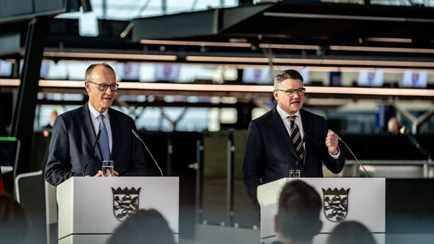 Zwei Männer stehen jeweils an einem Rednerpult am Frankfurter Flughafen.