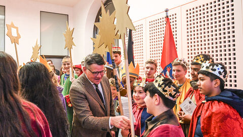 Ministerpräsident Boris Rhein zeigt auf den Stab eines Kindes, dass als Sternsinger gekleidet ist. Um sie herum stehen weitere Kinder als Sternsinger gekleidet.